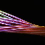 Close de cabos de fibra óptica multicoloridos sobre fundo escuro.